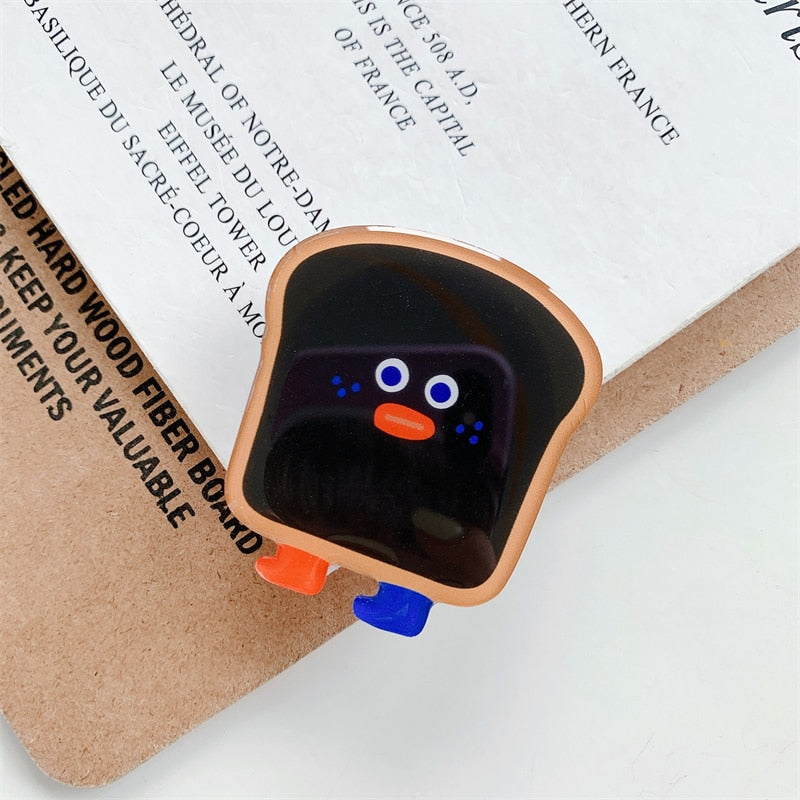 Black Toast Cartoon Phone Socket. Griptok. Attach it to your phone so you can hold it securely, prop it up whilst watching shows, or just fiddle around with it. Compatible with any phone!