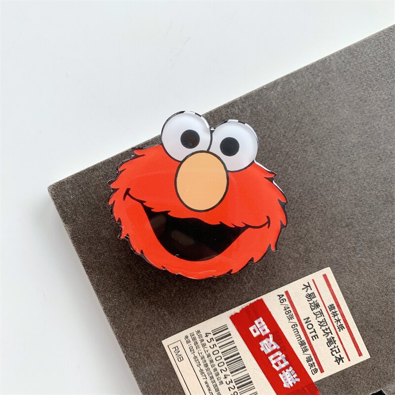 Elmo Cartoon Phone Socket. Griptok. Attach it to your phone so you can hold it securely, prop it up whilst watching shows, or just fiddle around with it. Compatible with any phone!
